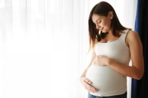 Pregnant woman standing indoors holding lower front