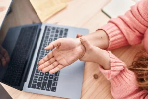 Woman experiencing carpal tunnel pain while using laptop