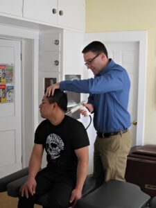 Dr. Russell Brokstein performing a chiropractic adjustment on a patient seated in an examination room.