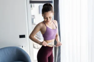 Sporty young woman and measure around her body at home